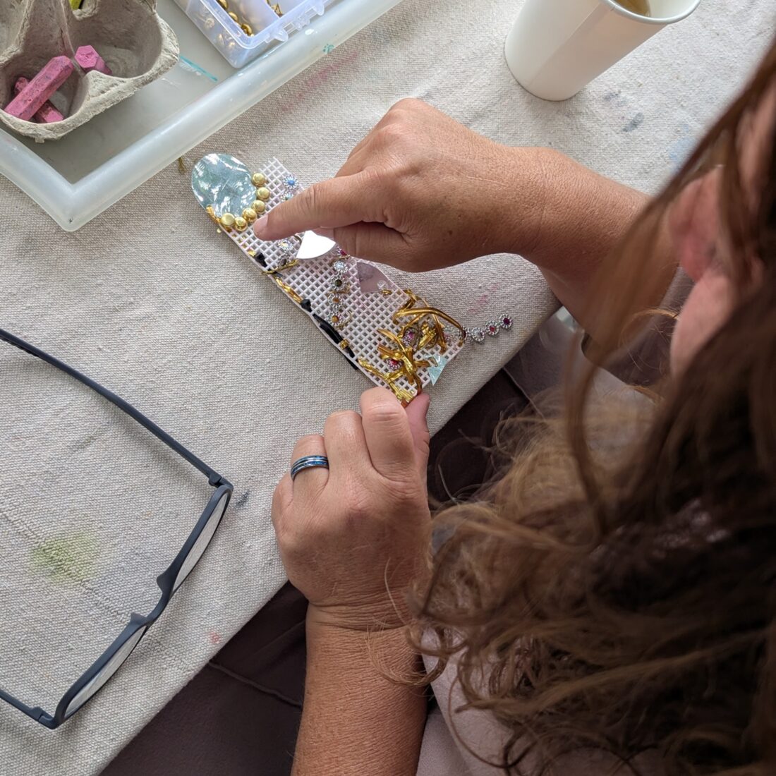 A woman adding gold beads and gems to a mixed-media art piece during a Creative Hour workshop at Pachis art studio, Linda Vista, San Diego